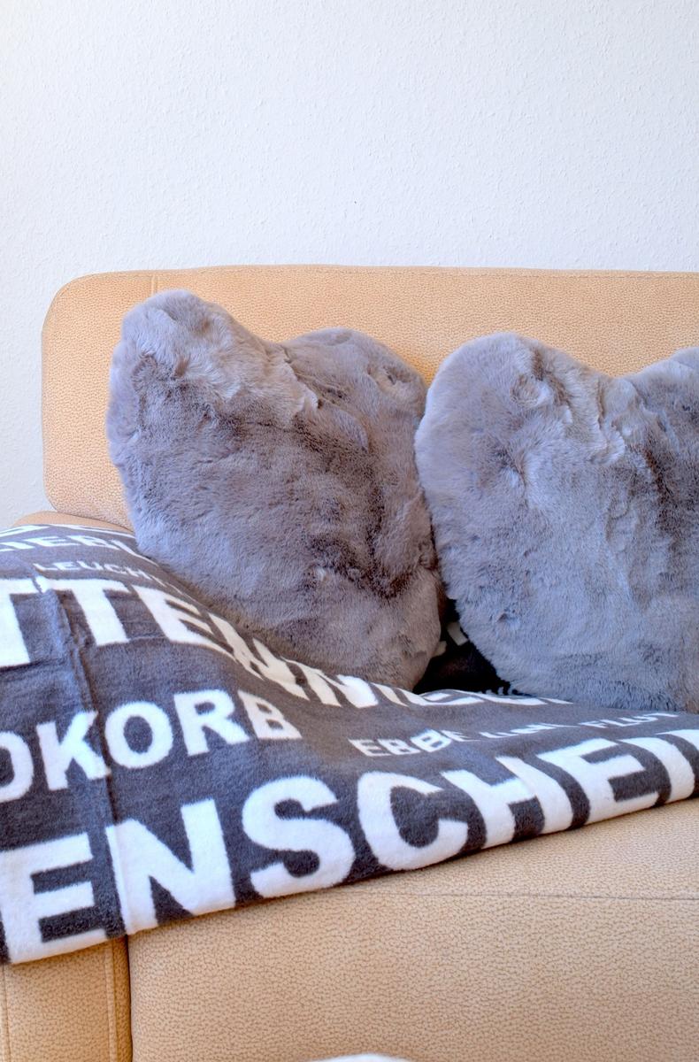 Beige Sofa mit zwei grauen Kissen und einer gemusterten Decke.
