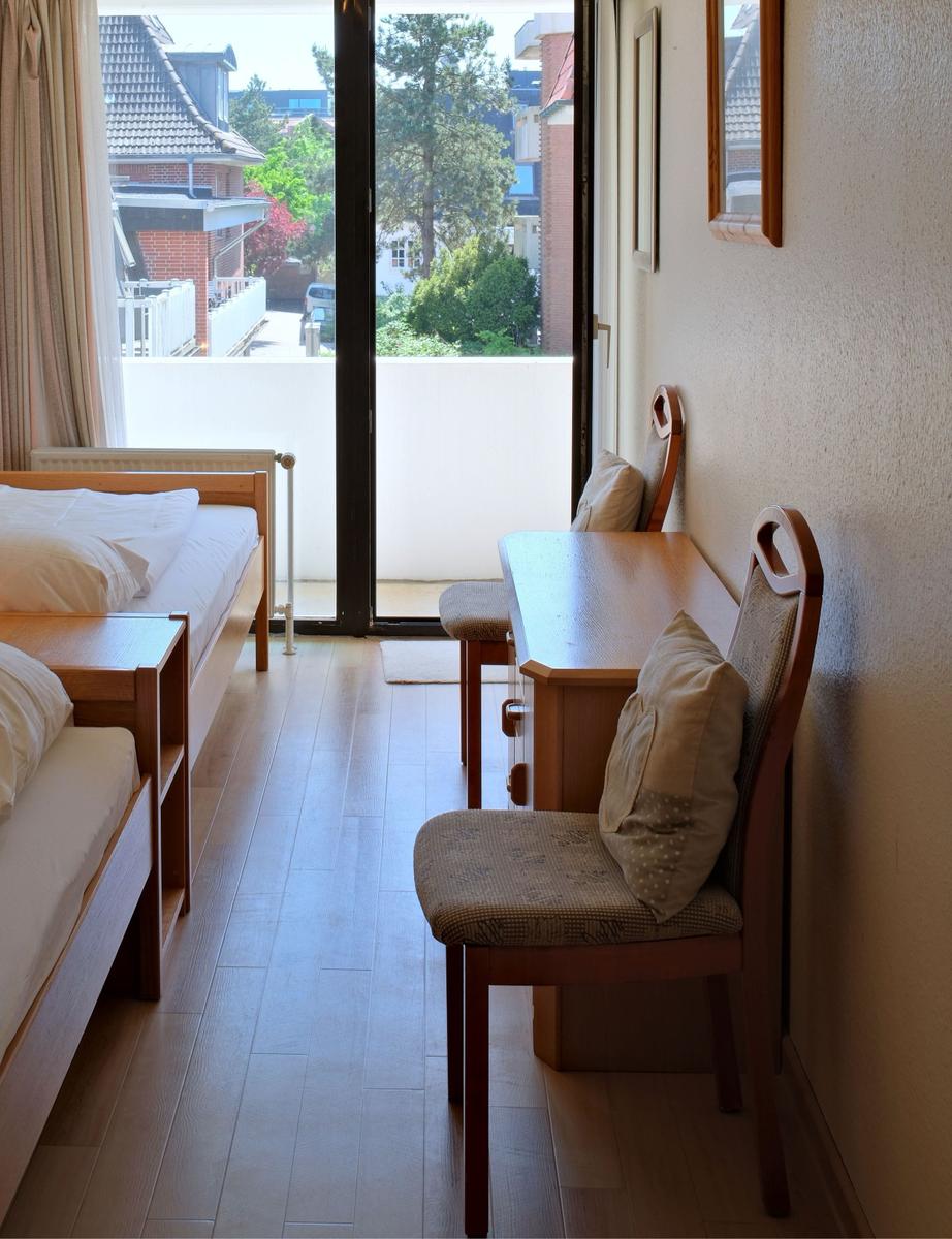 Zimmer mit Bett, Tisch und Stühlen. Durchgang zur Terrasse mit Blick auf Wohngebiet.