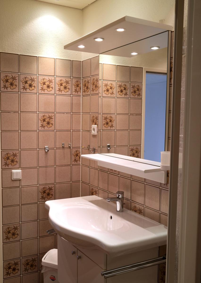 Badezimmer mit Spiegel, Waschbecken und floralen Fliesen.