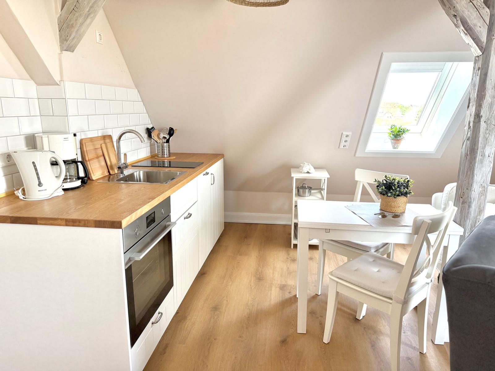 Küche mit Essbereich unter Dachschrägen. Holzfußboden, weiße Möbel und Fenster.