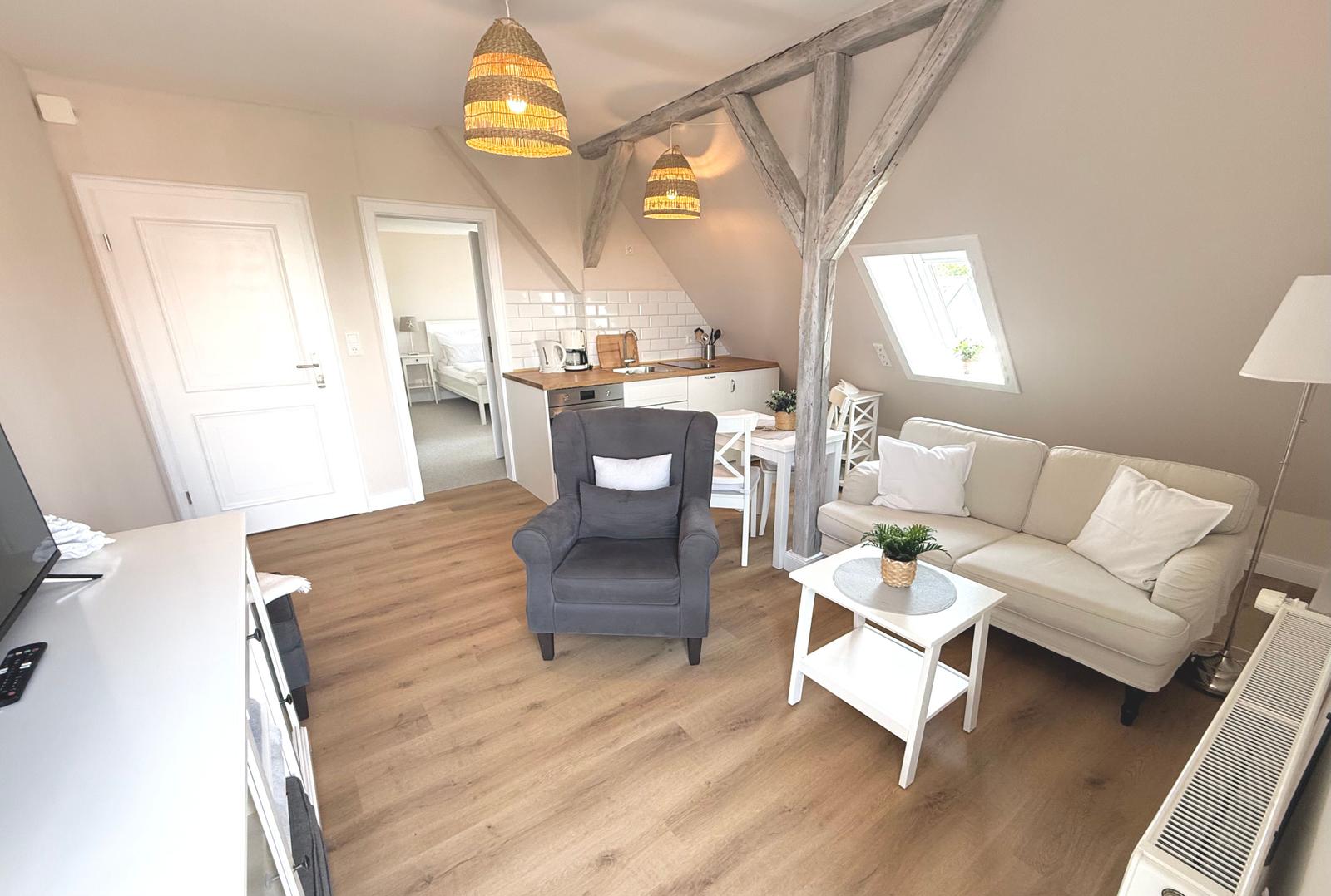 Wohnbereich mit Sofa, Sessel, Esstisch und Küchenzeile unter Holzbalken.