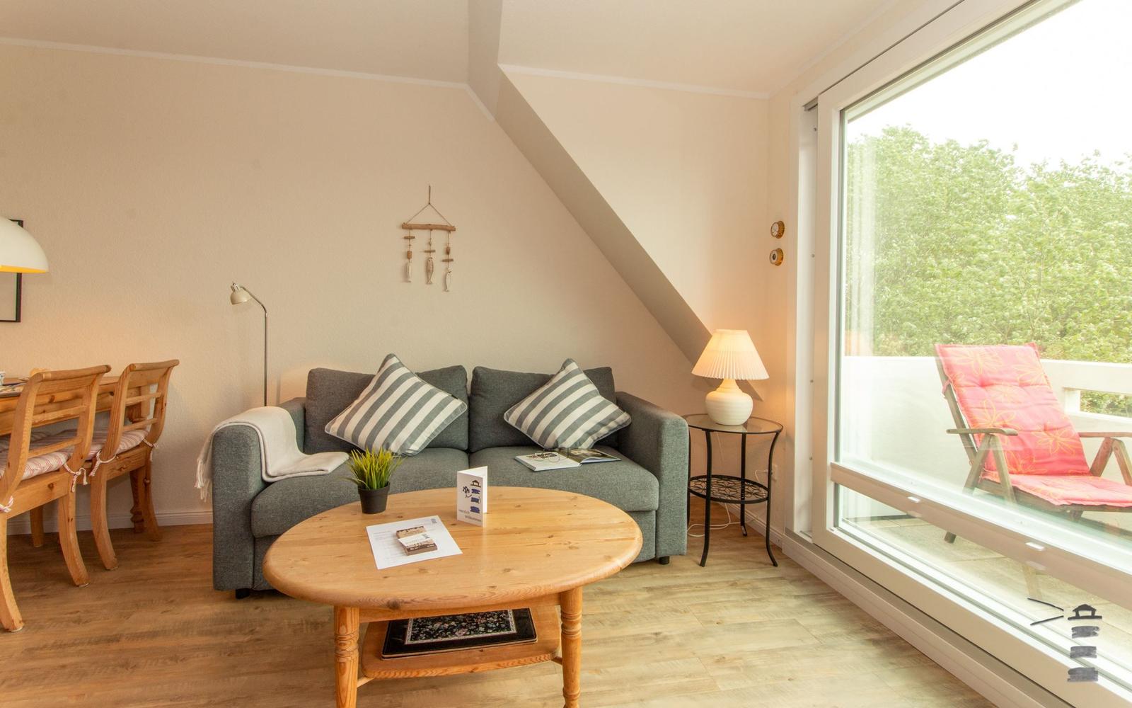 Wohnzimmer mit Sofa, Tisch und Blick auf Balkon mit Stuhl.