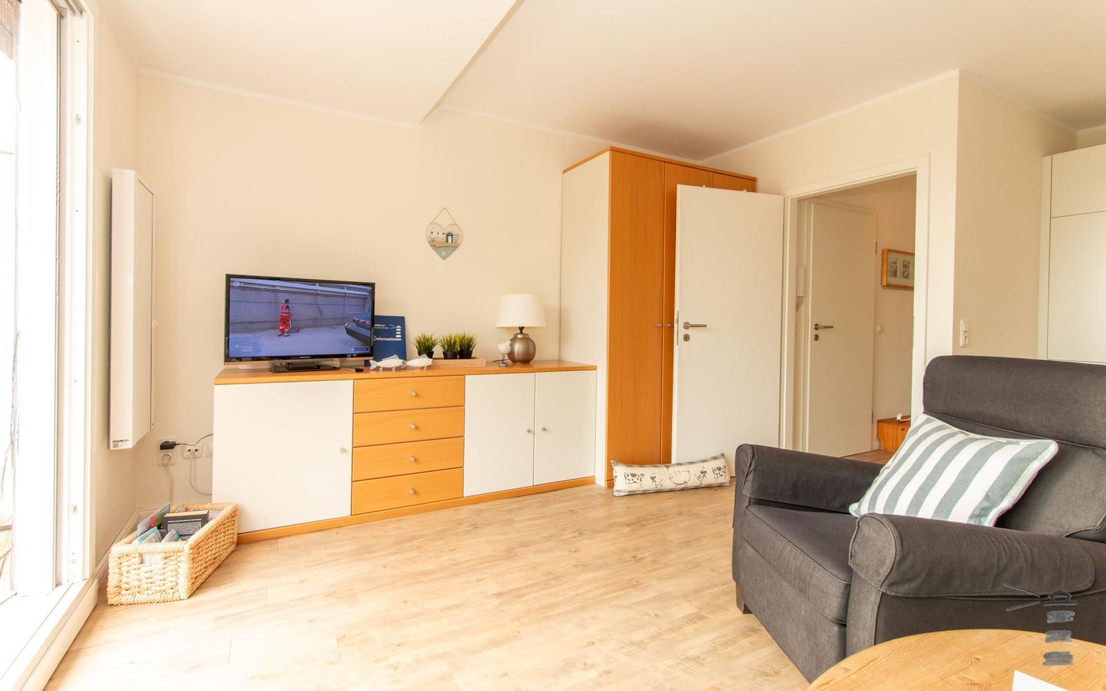 Wohnzimmer mit Sofa, TV und Holzboden. Tür führt in andere Räume.