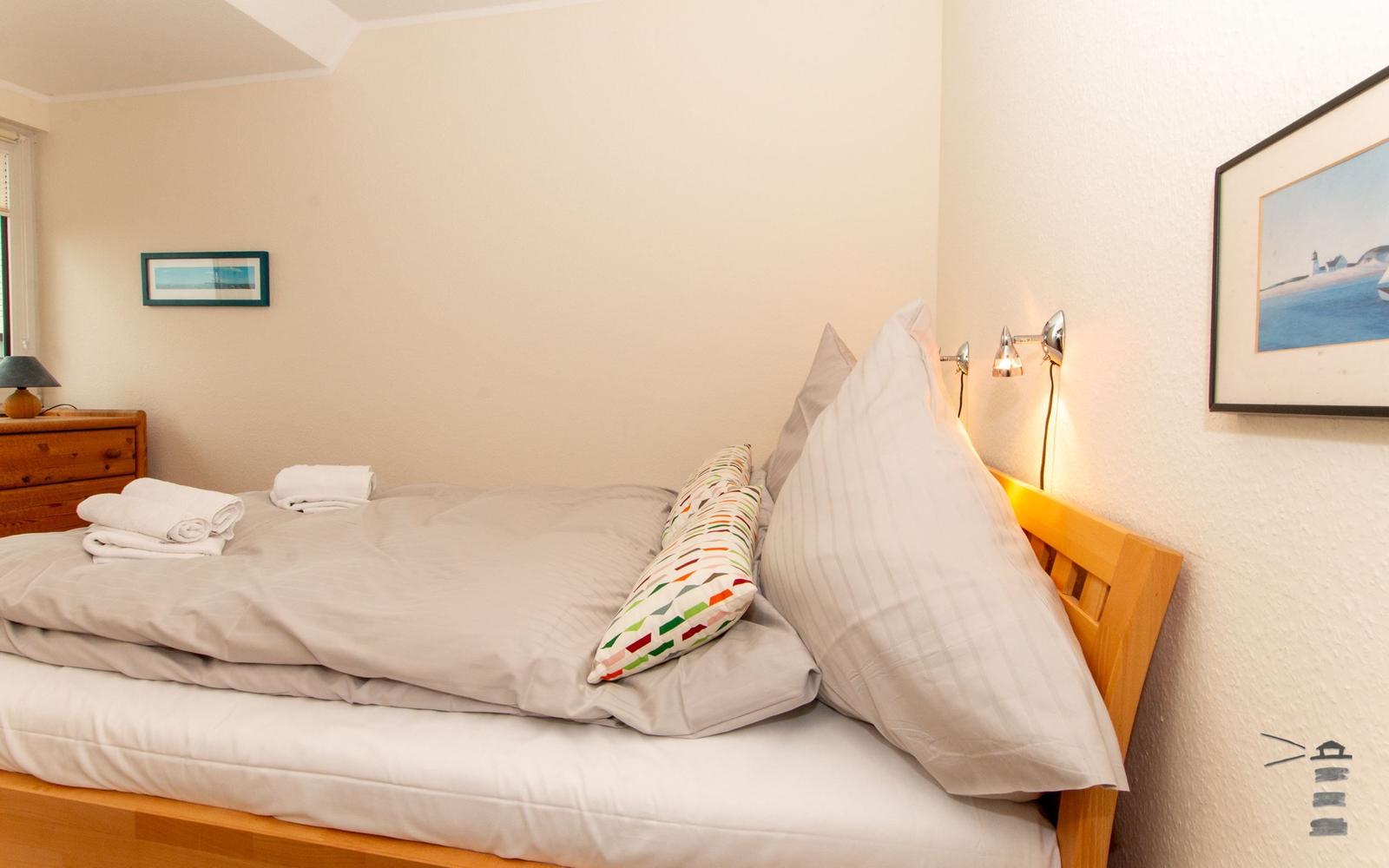 Schlafzimmer mit Bett, Kissen, Handtüchern und Wandbildern.