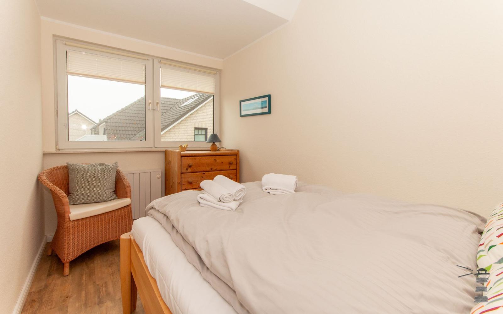 Schlafzimmer mit Bett, Nachttisch, Stuhl und Fenster.