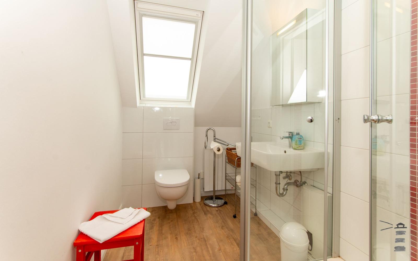 Badezimmer mit Dusche, Waschbecken und Toilette unter Dachschräge mit Fenster.