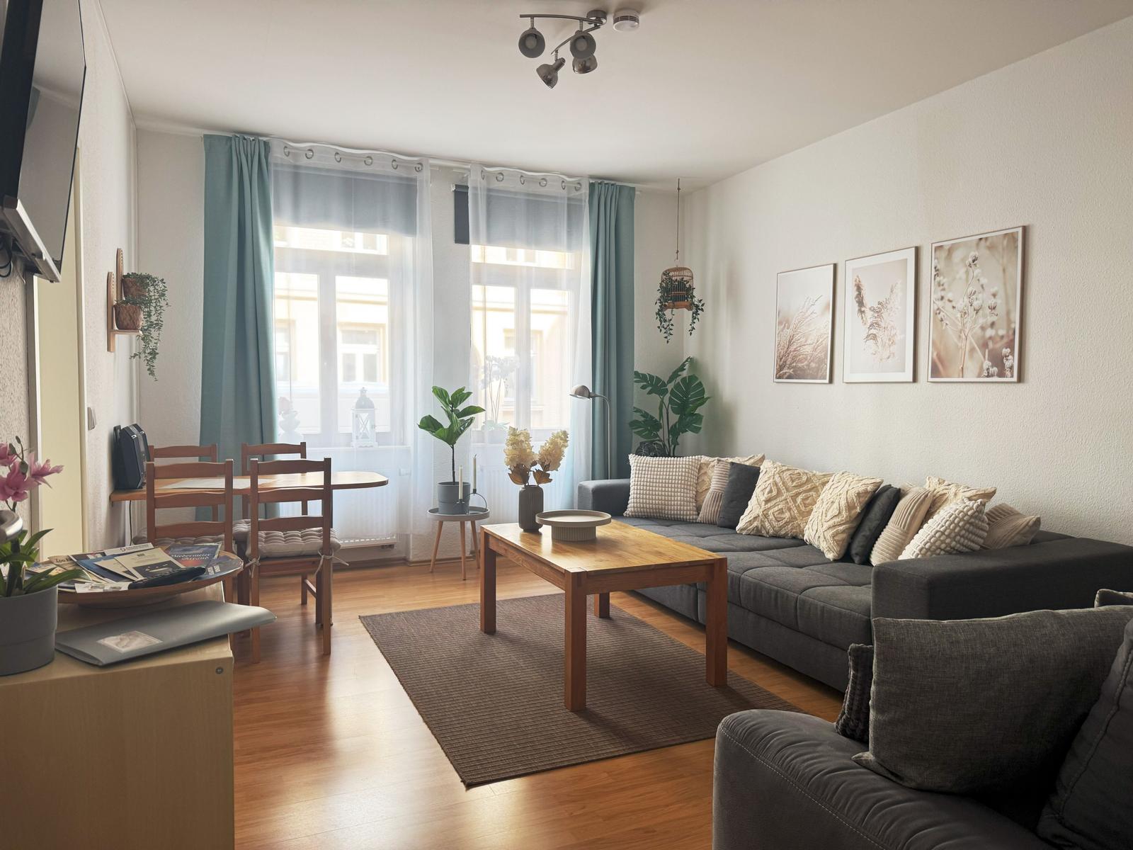 Wohnzimmer mit Sofa, Tisch und Fenster. Zimmer mit Holzboden und Pflanzen.
