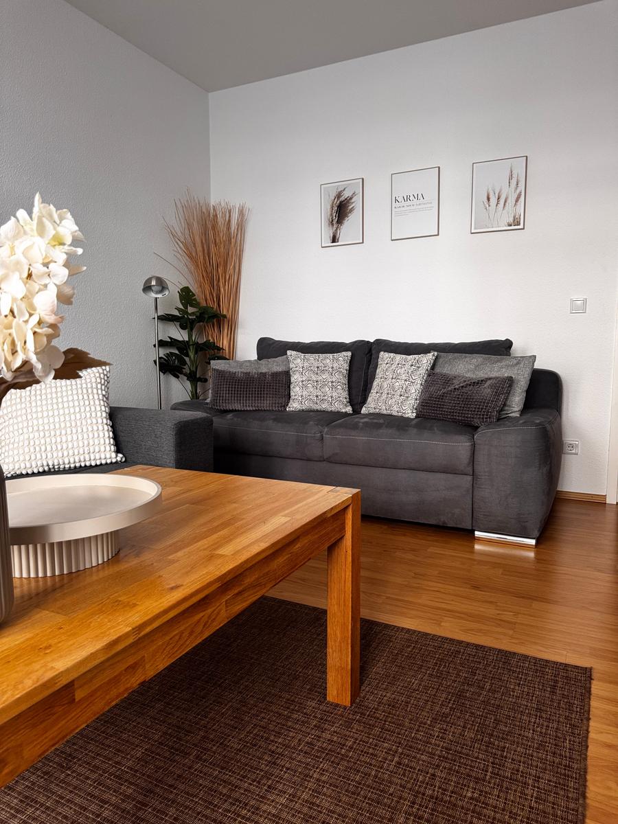 Ein Wohnzimmer mit grauem Sofa, Holztisch und Wandbildern.