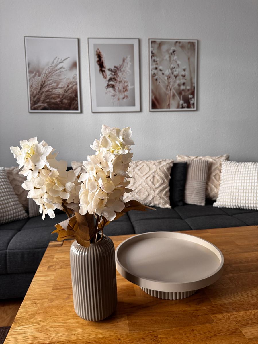 Ein Wohnzimmer mit dunklem Sofa, Holztisch und Blumen in einem Vasen.