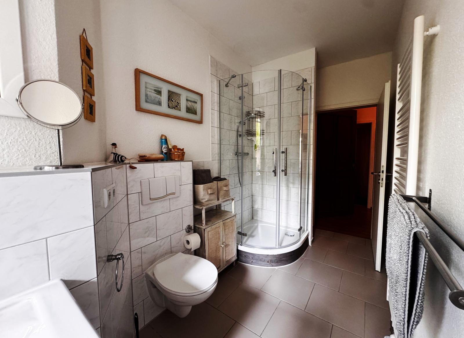 Badezimmer mit Dusche, Toilette und Waschbecken. Wandverkleidung und Bodenfliesen.