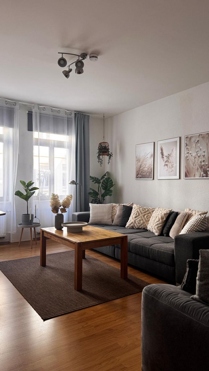 Wohnzimmer mit grauem Sofa, Holztisch und Pflanzen an Fenster