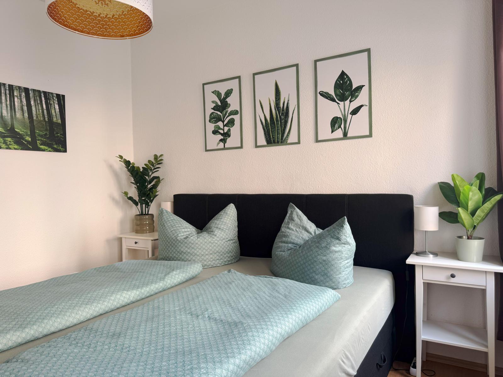 Schlafzimmer mit Bett, Nachttischen und Pflanzen an der Wand.