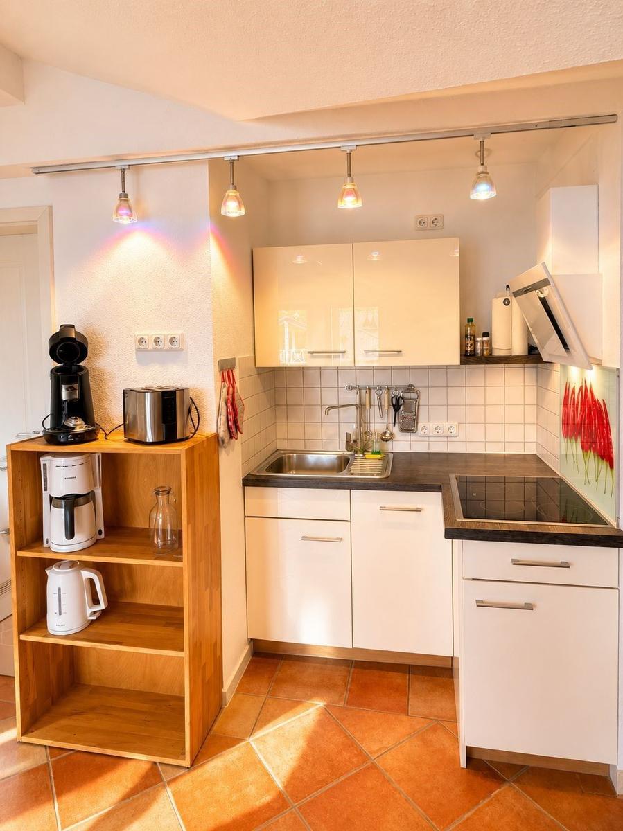 Küche mit weißen Schränken, Edelstahlspüle und Holzregal mit Küchengeräten.