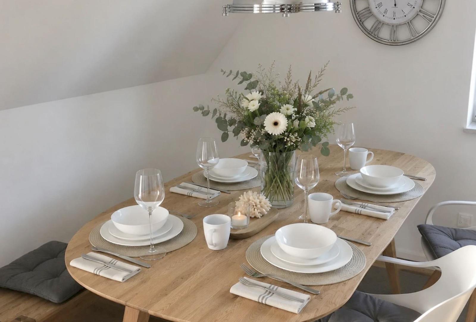 Ein gedeckter Holztisch mit weißen Geschirr und Blumendekoration.