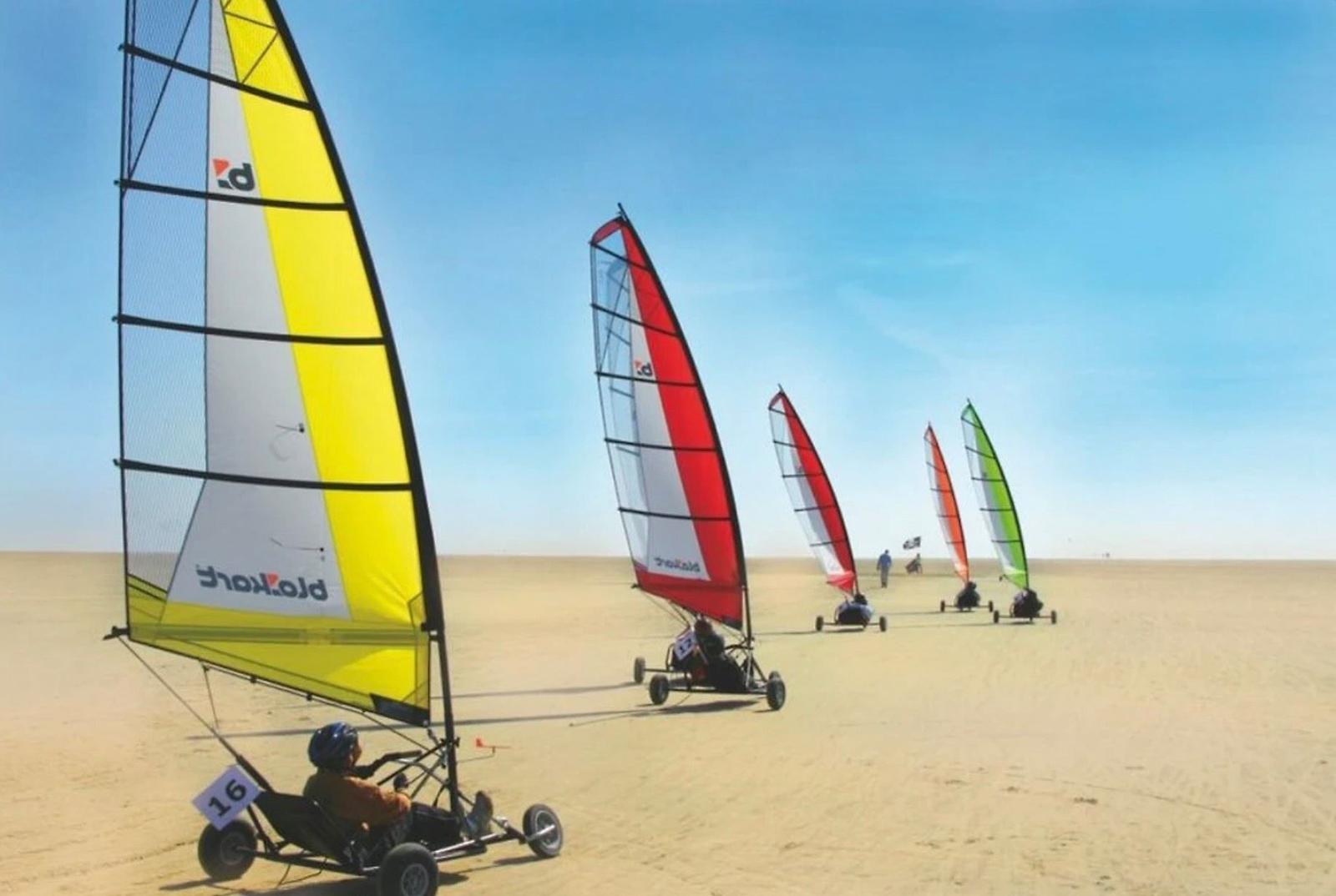 Sailbikes auf Sand mit bunten Segeln unter blauem Himmel.