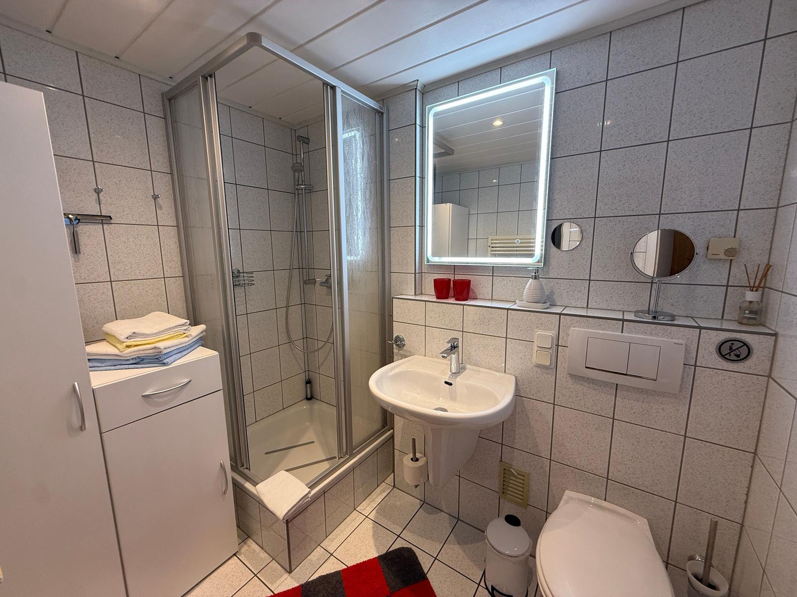 Bad mit Toilette, Dusche und Waschbecken mit beleuchtetem Spiegel.