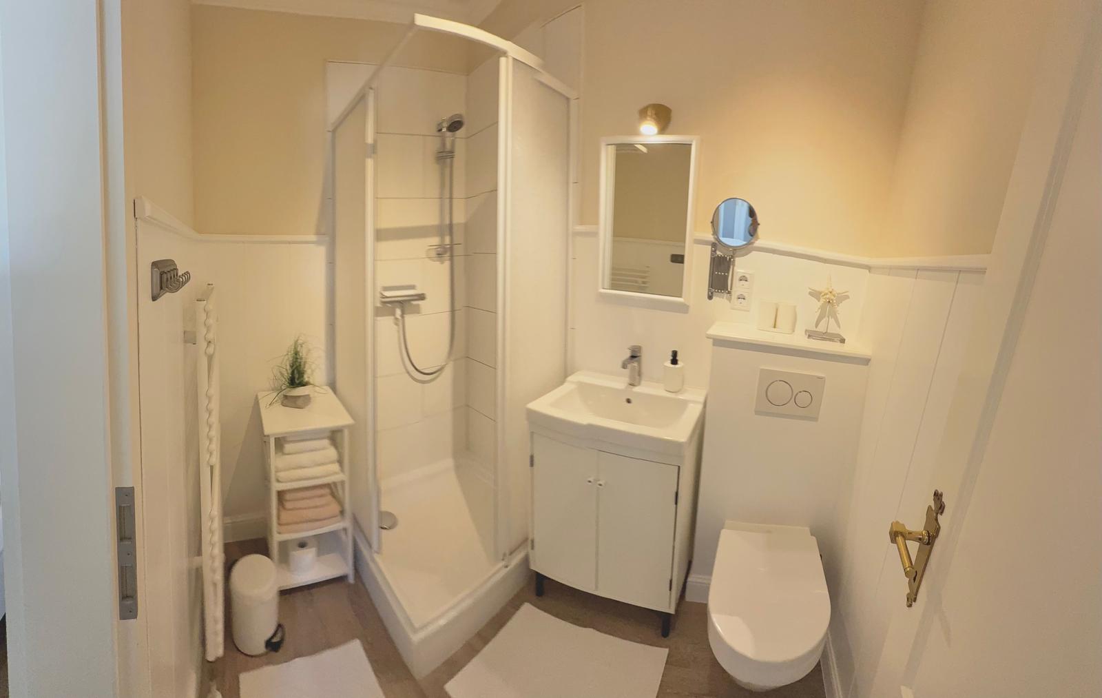 Badezimmer mit Dusche, Waschbecken und Toilette. Weiße Einrichtung und Spiegel.