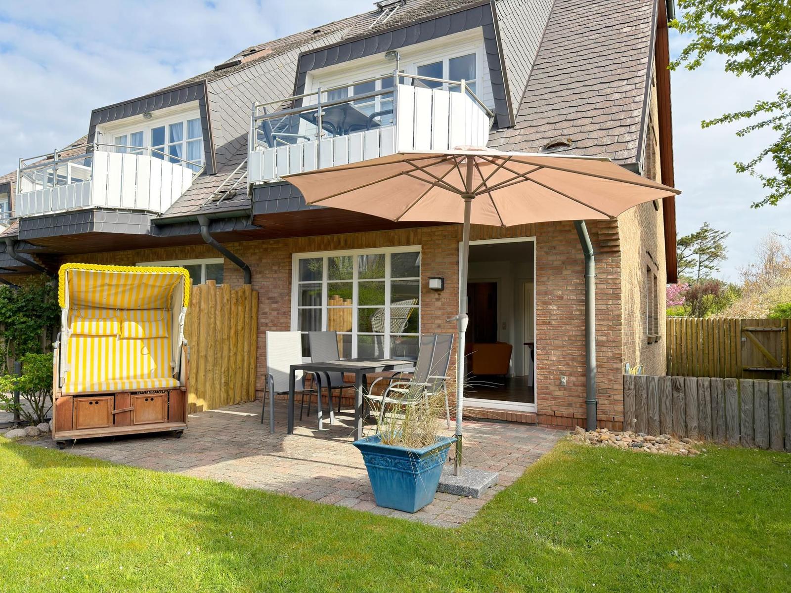 Haus mit Terrasse, Sonnenschirm und Strandkorb im Garten.
