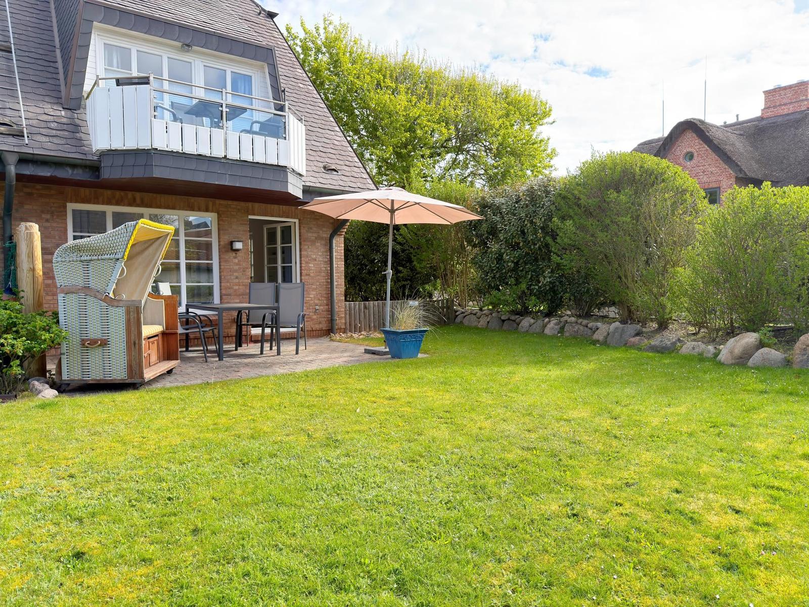 Hinterhof mit grünem Rasen, Terrasse, Sonnenschirm und Strandkorb.