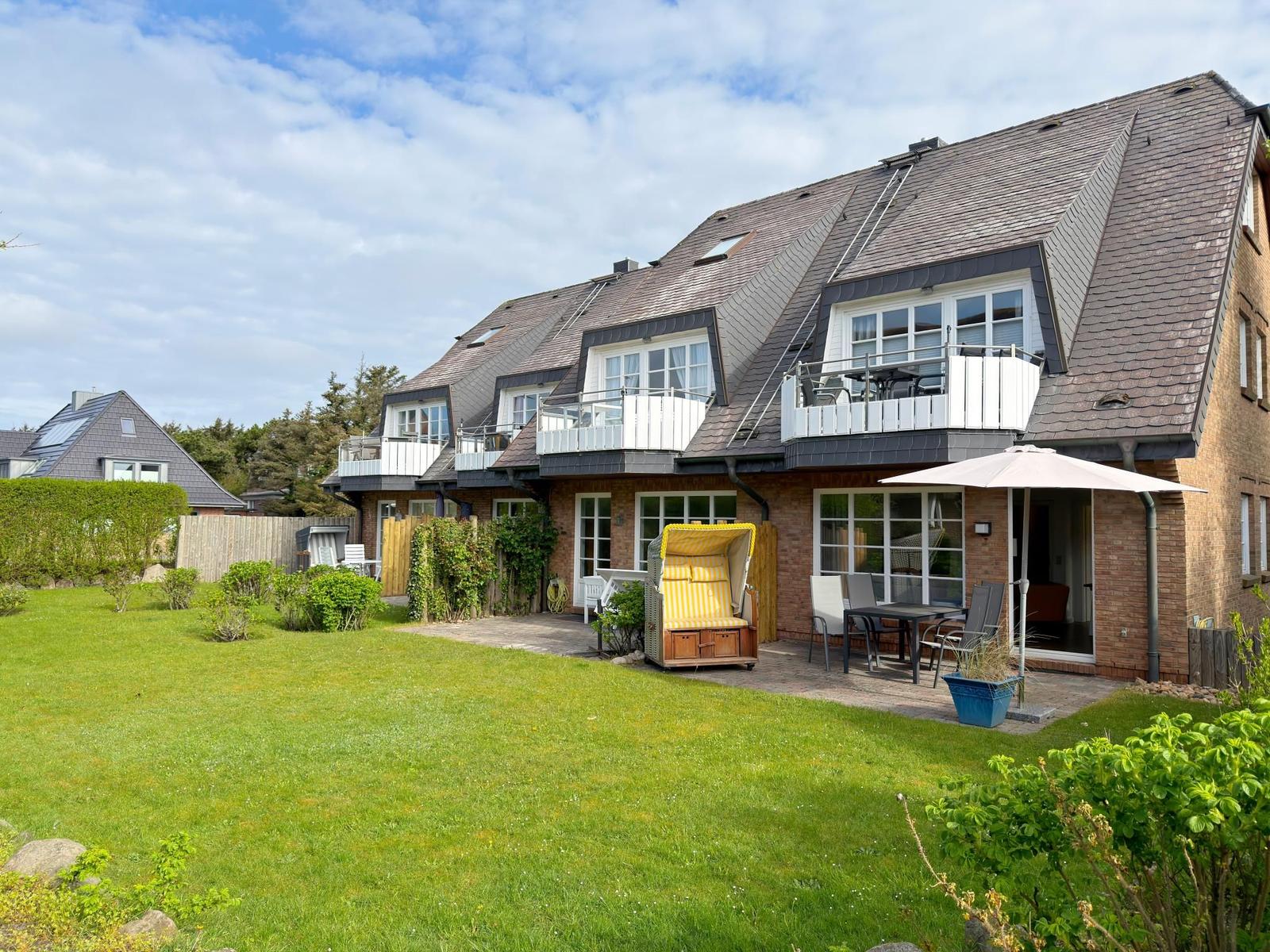 Haus mit Balkonen, Garten und Liegestuhl im Freien.