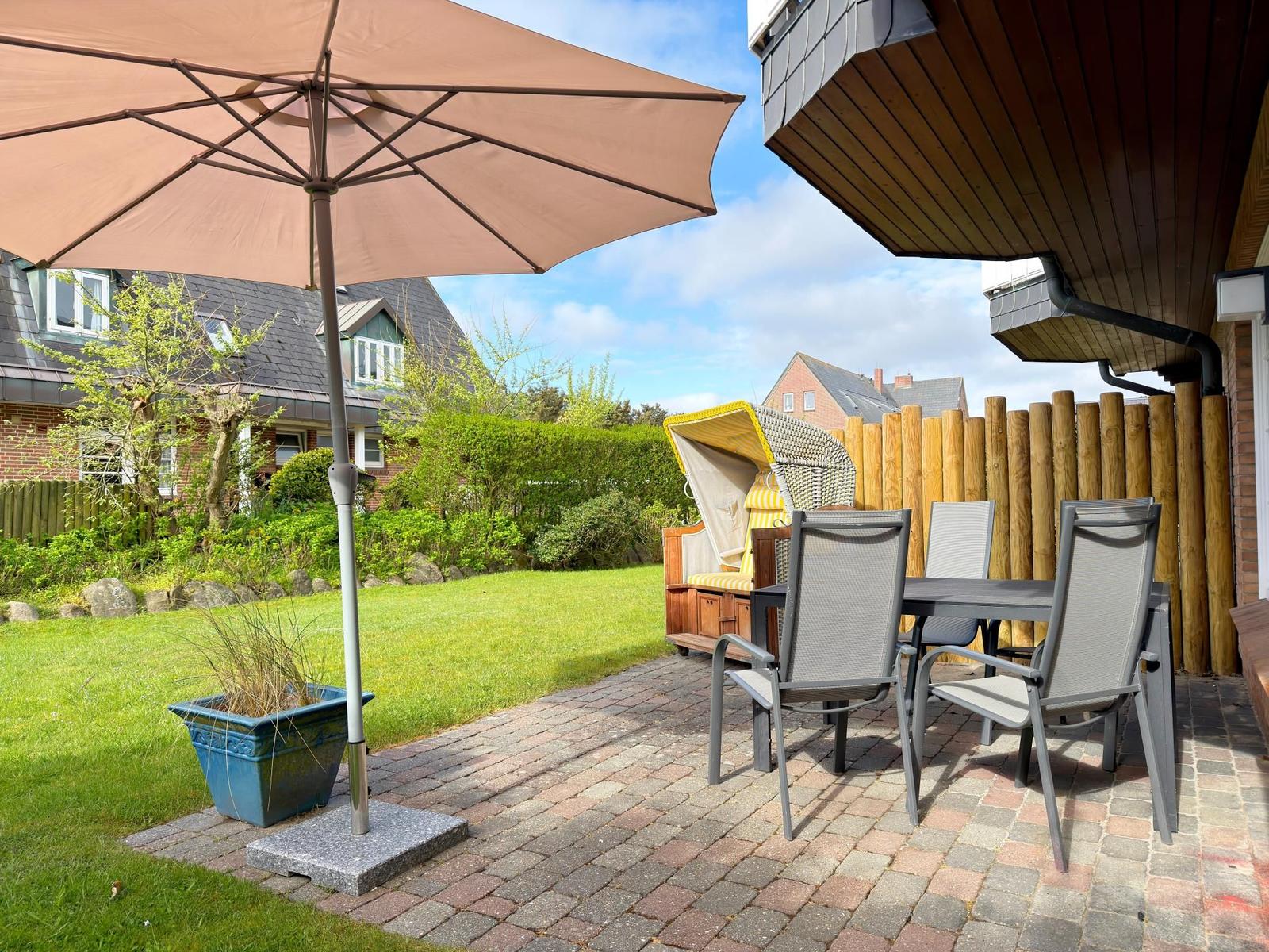 Terrasse mit Tisch, Stühlen und Sonnenschirm. Hinterhof mit Grünfläche und Holzzaun.