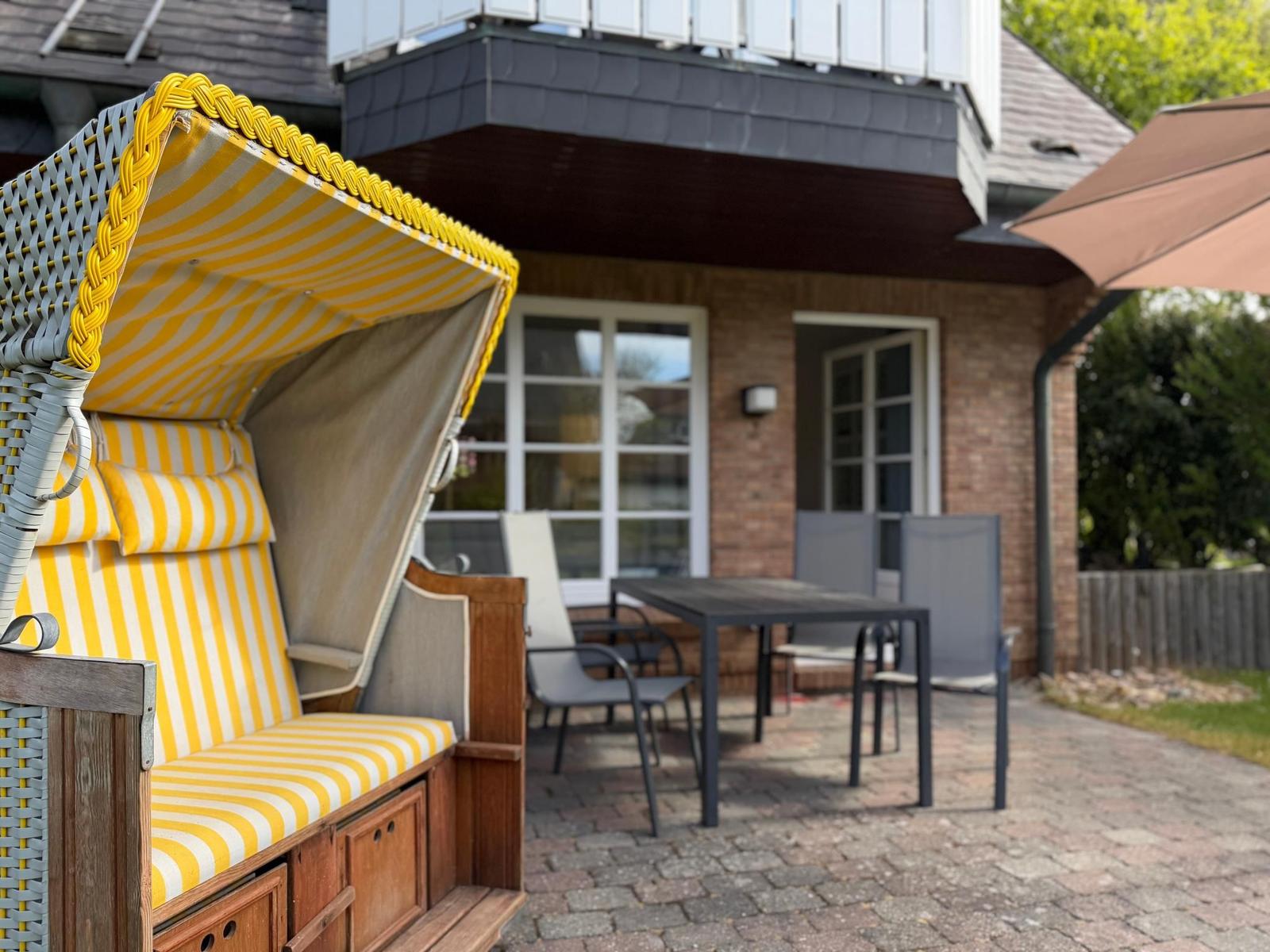 Terrasse mit Strandkorb, Tisch und Stühlen vor einem Haus mit Backsteinfassade.