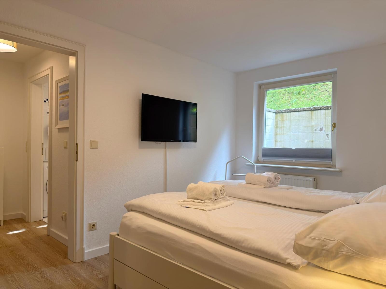 Zimmer mit Bett, Fernseher und Fenster. Flur mit Tür und Bild an der Wand.