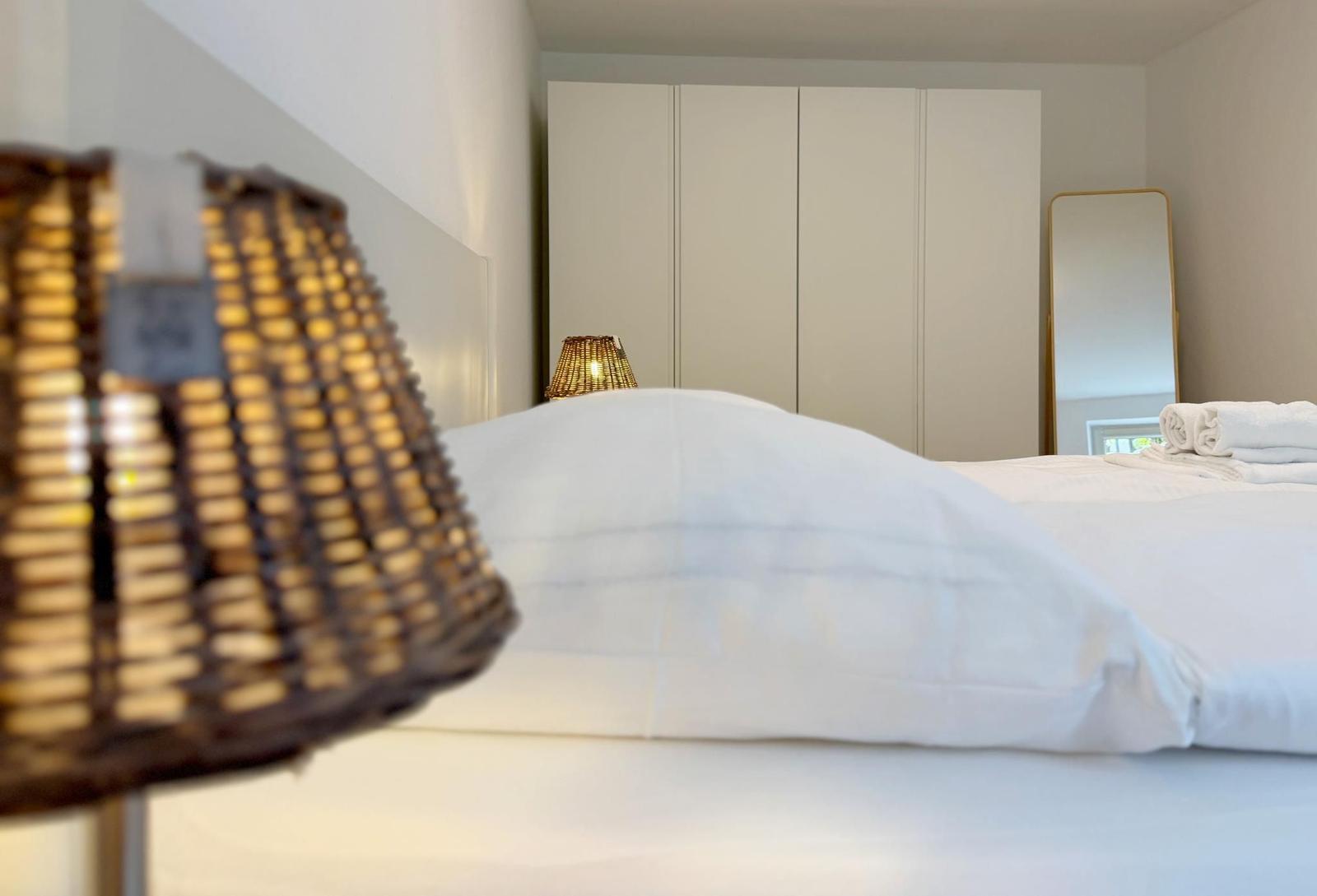 Schlafzimmer mit weißem Bett, Kleiderschrank und Spiegel