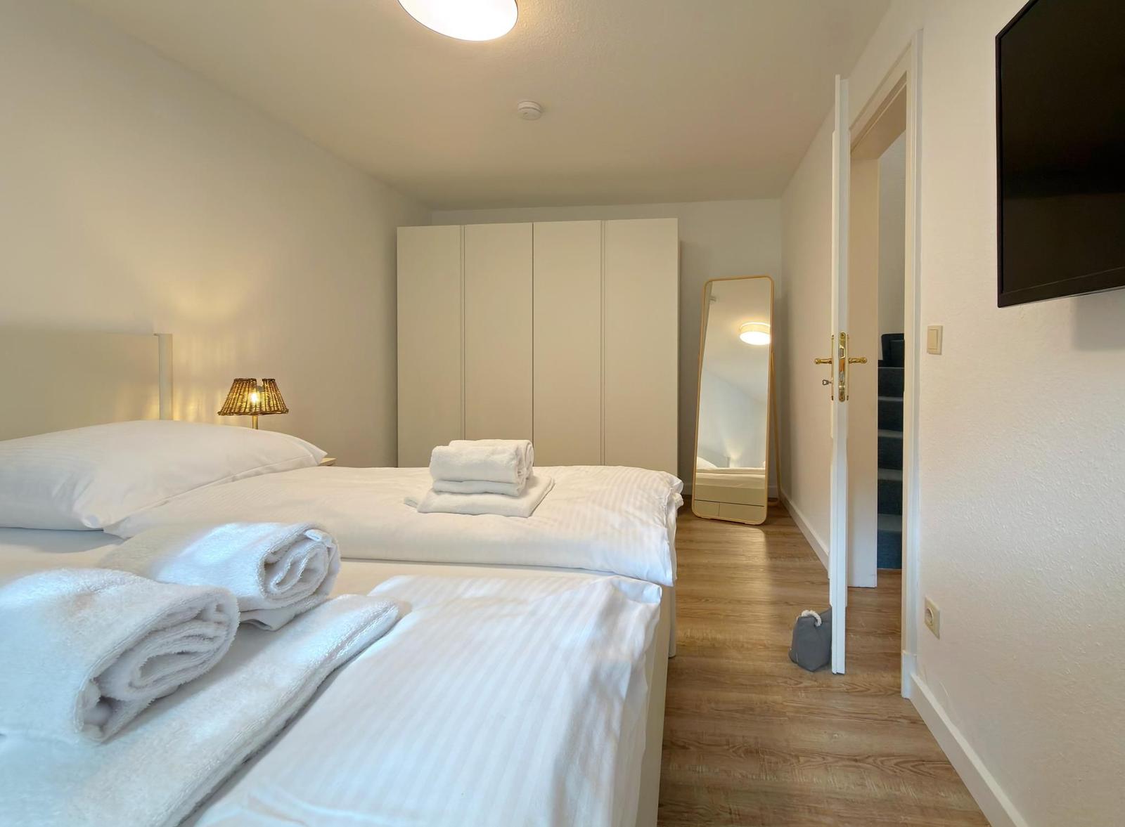 Zimmer mit Doppelbett, Kleiderschrank, Spiegel und Fernseher an der Wand.