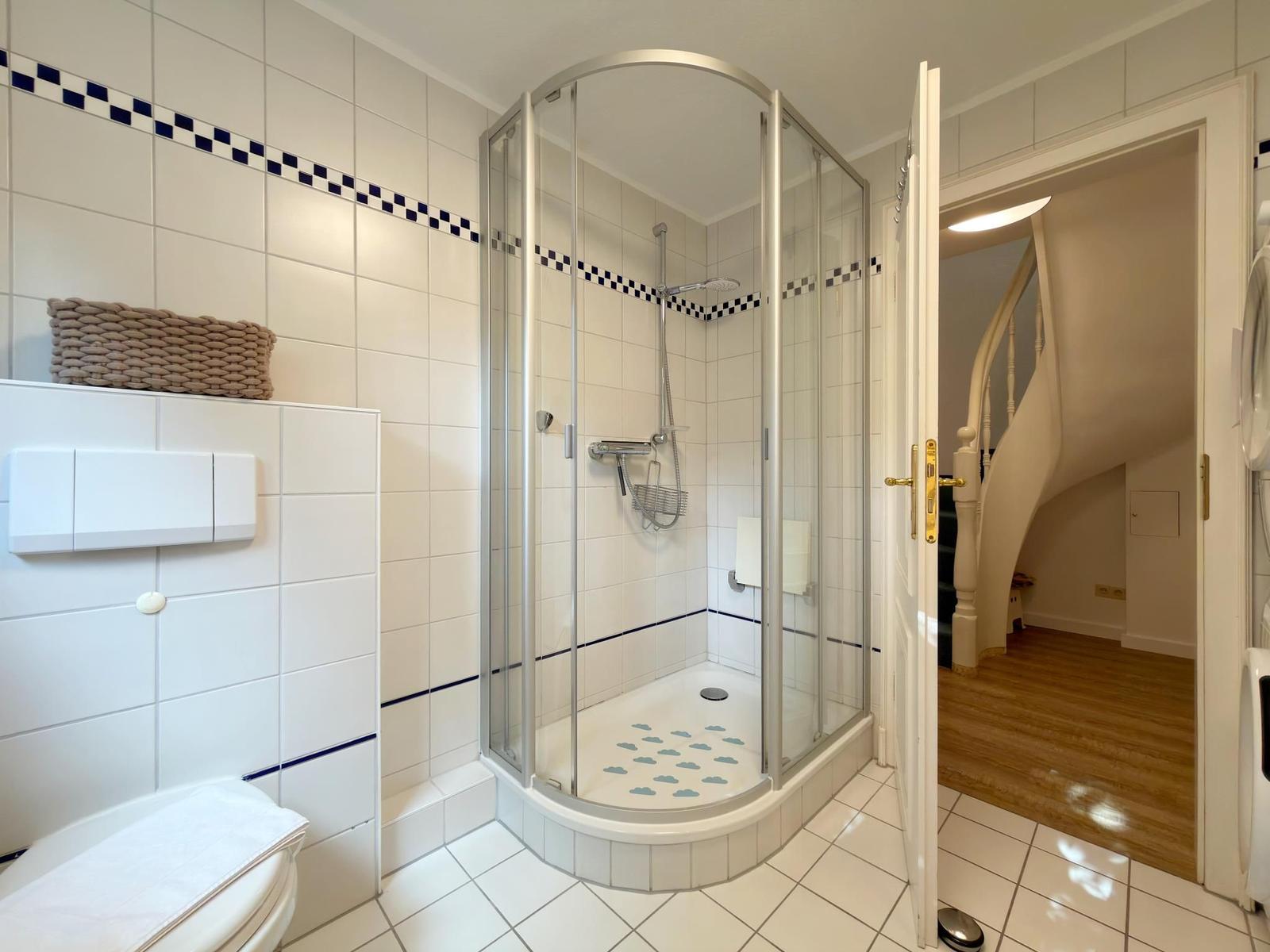 Badezimmer mit Dusche, Toilette und Blick in die Treppe.