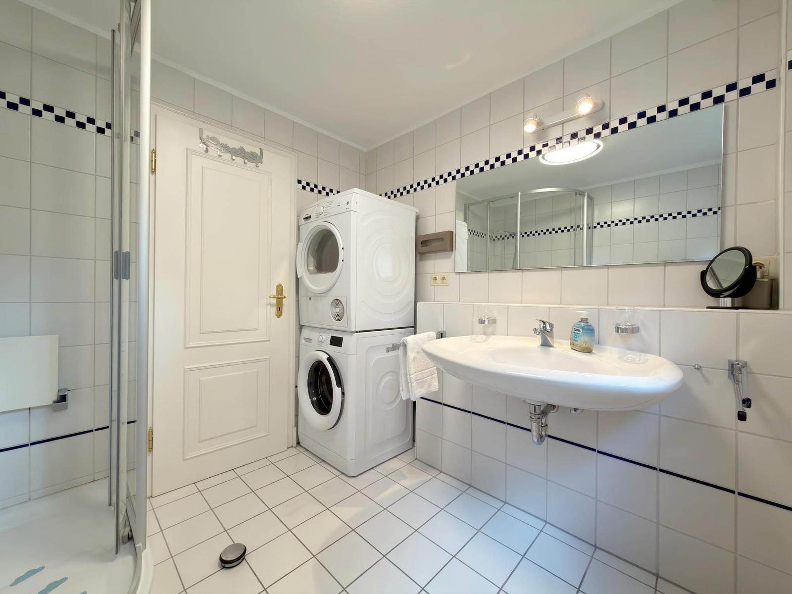 Badezimmer mit Waschmaschine, Spiegel und Dusche.