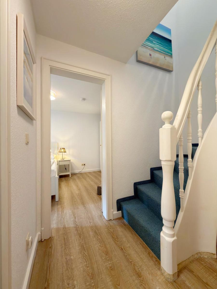 Flur mit Holzboden, Treppe mit blauem Teppich und Blick in Schlafzimmer