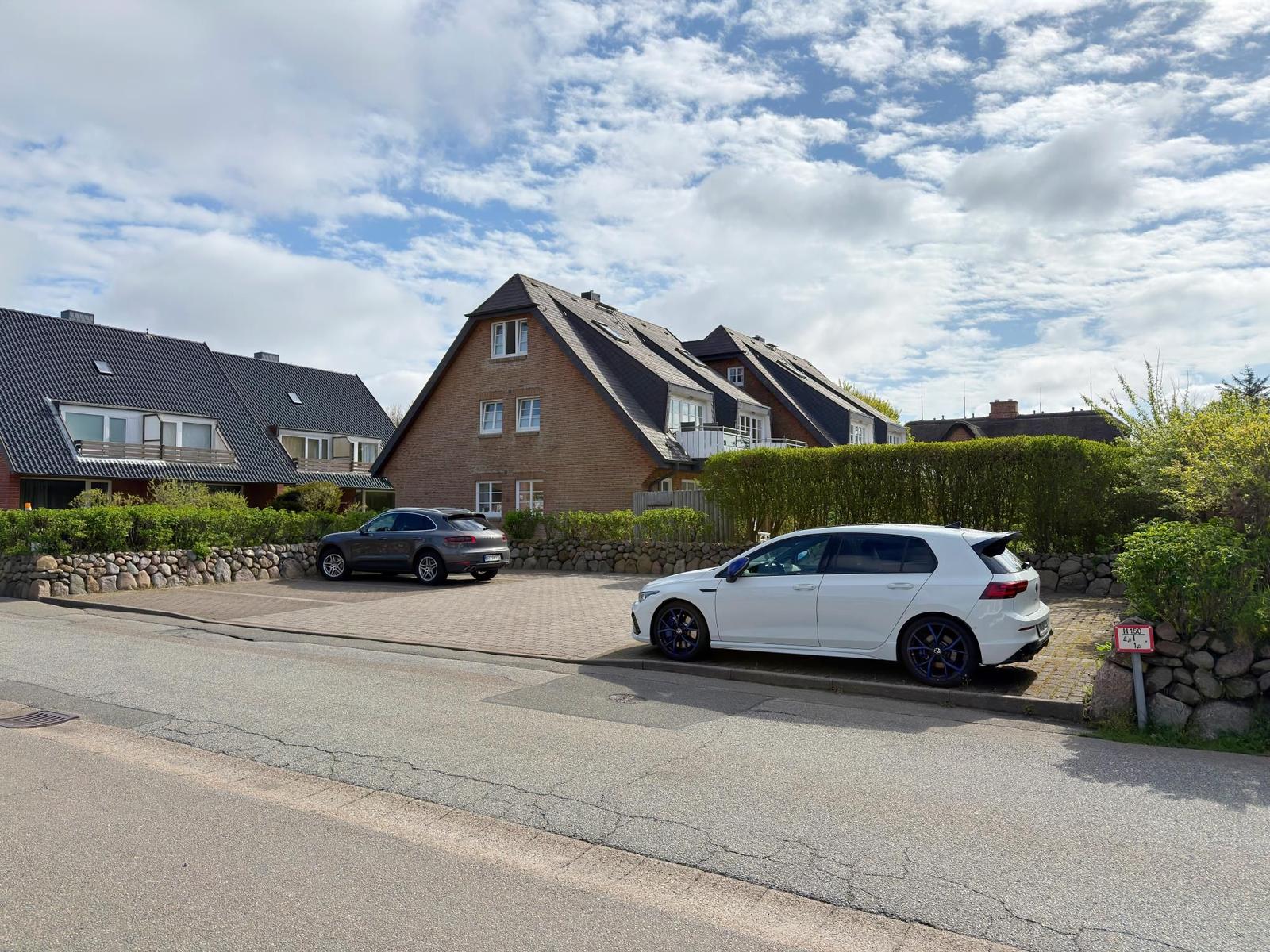 Zwei Autos parken vor einem Haus mit Steinmauer und Hecke.