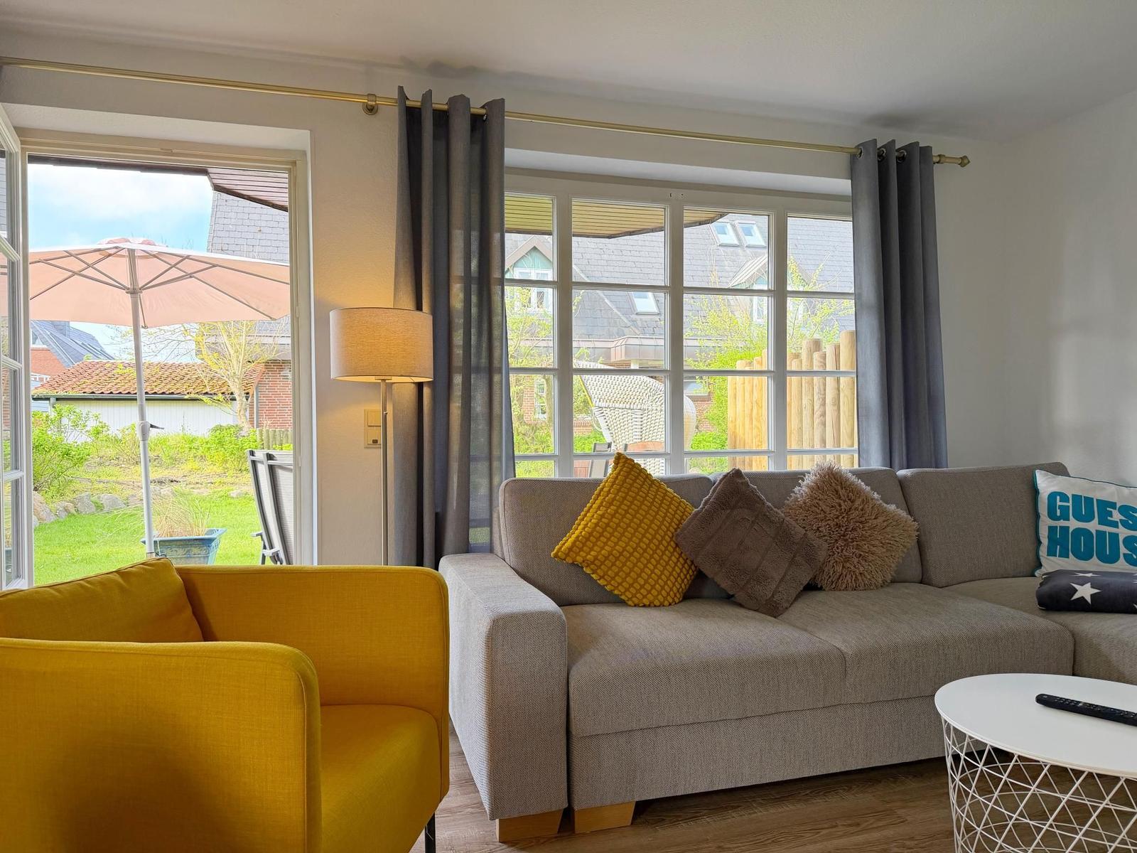 Wohnzimmer mit Sofa, gelber Sessel und Blick auf Garten