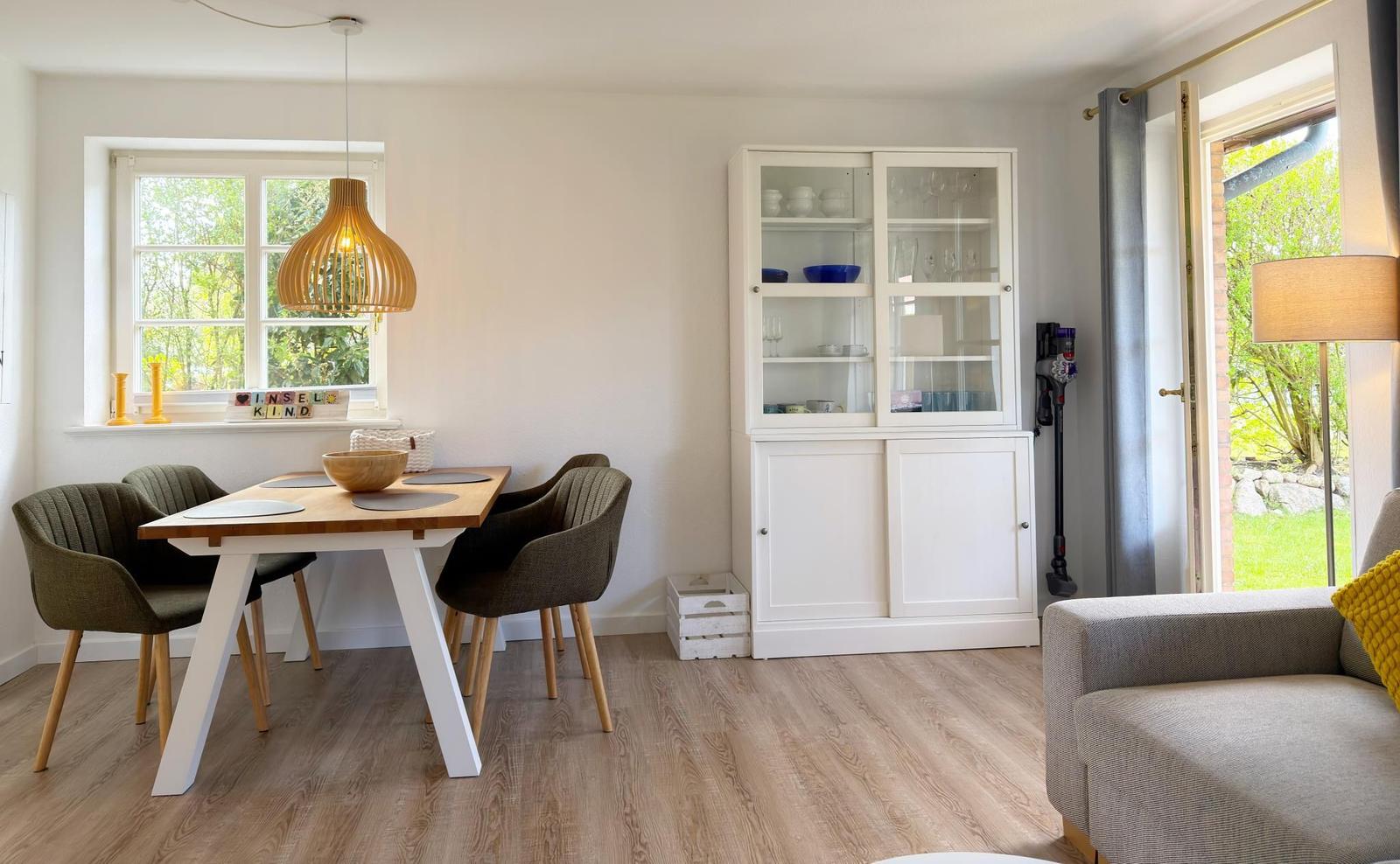 Essbereich mit Tisch, Stühlen und Glaswand-Schrank. Fenster und Tür zur Außenanlage.