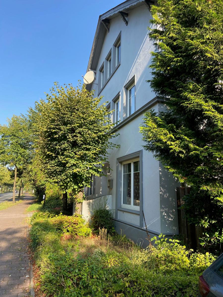 Ein zweistöckiges Haus mit Fenstern und einem Satellitenschüssel. Umgeben von Bäumen und Grünflächen.
