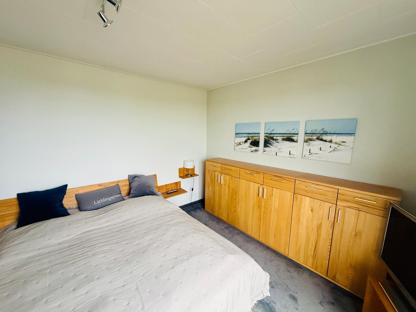 Schlafzimmer mit Bett, Holzschrank und Strandbildern an der Wand.