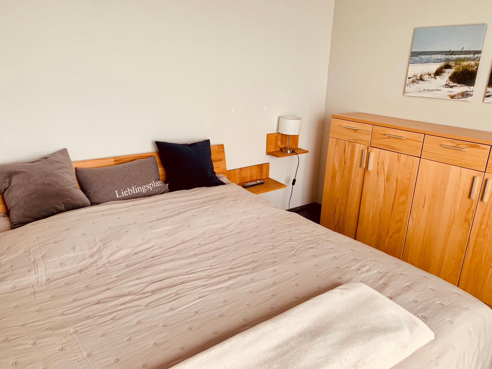 Schlafzimmer mit Bett, Nachttisch und Kleiderschrank. Wandbild zeigt Strand.