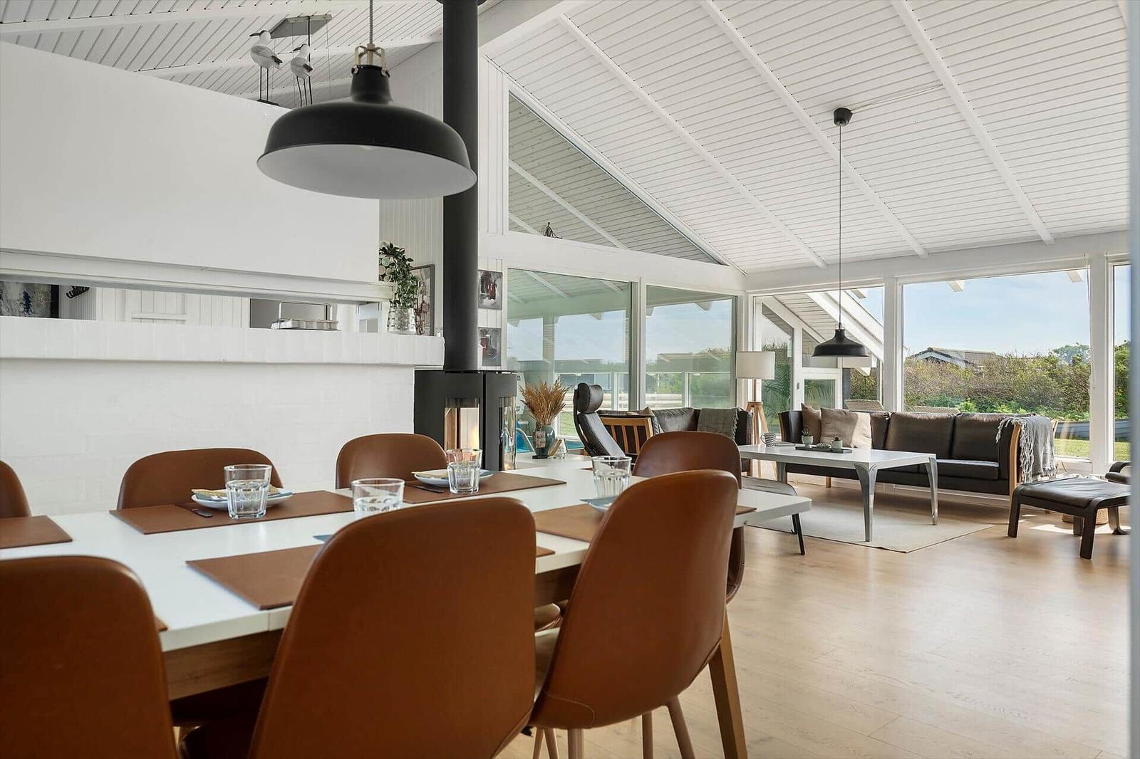 Dining area with brown chairs and living room with sofa and large windows.