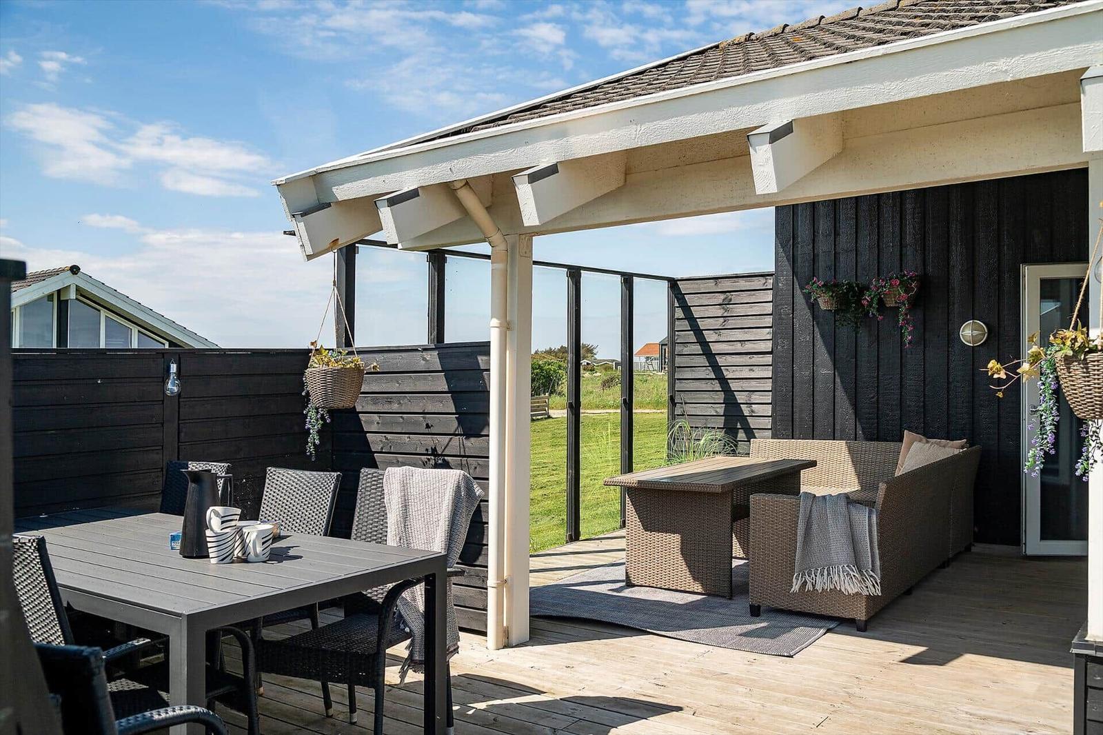 Terrace with seating and table under roof. Black wooden walls and hanging flowers.