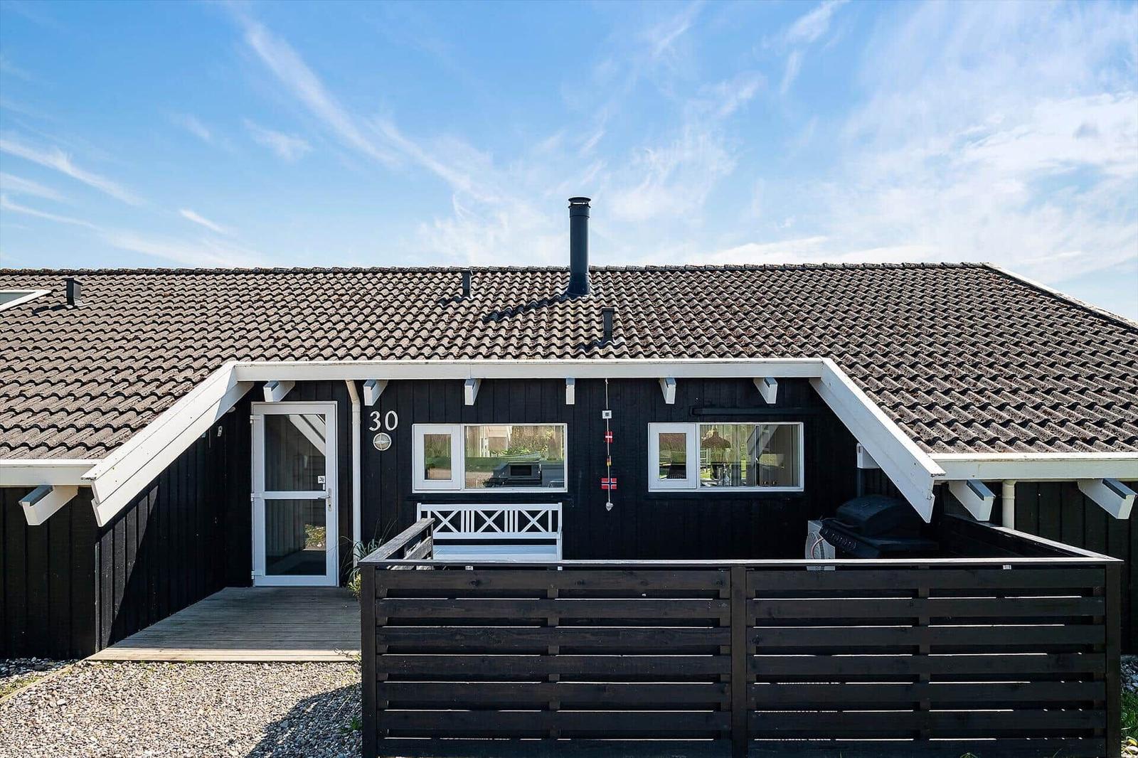 Black house with wooden porch and tiled roof. House number 30.