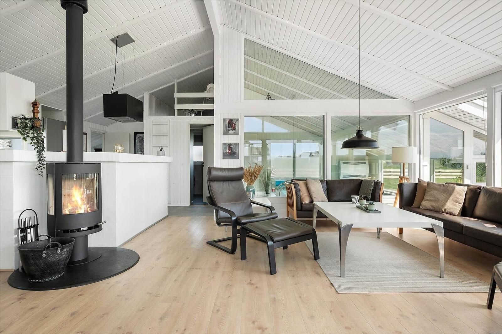 Living area with fireplace, leather sofa, and wooden floor. Large windows and white ceiling.