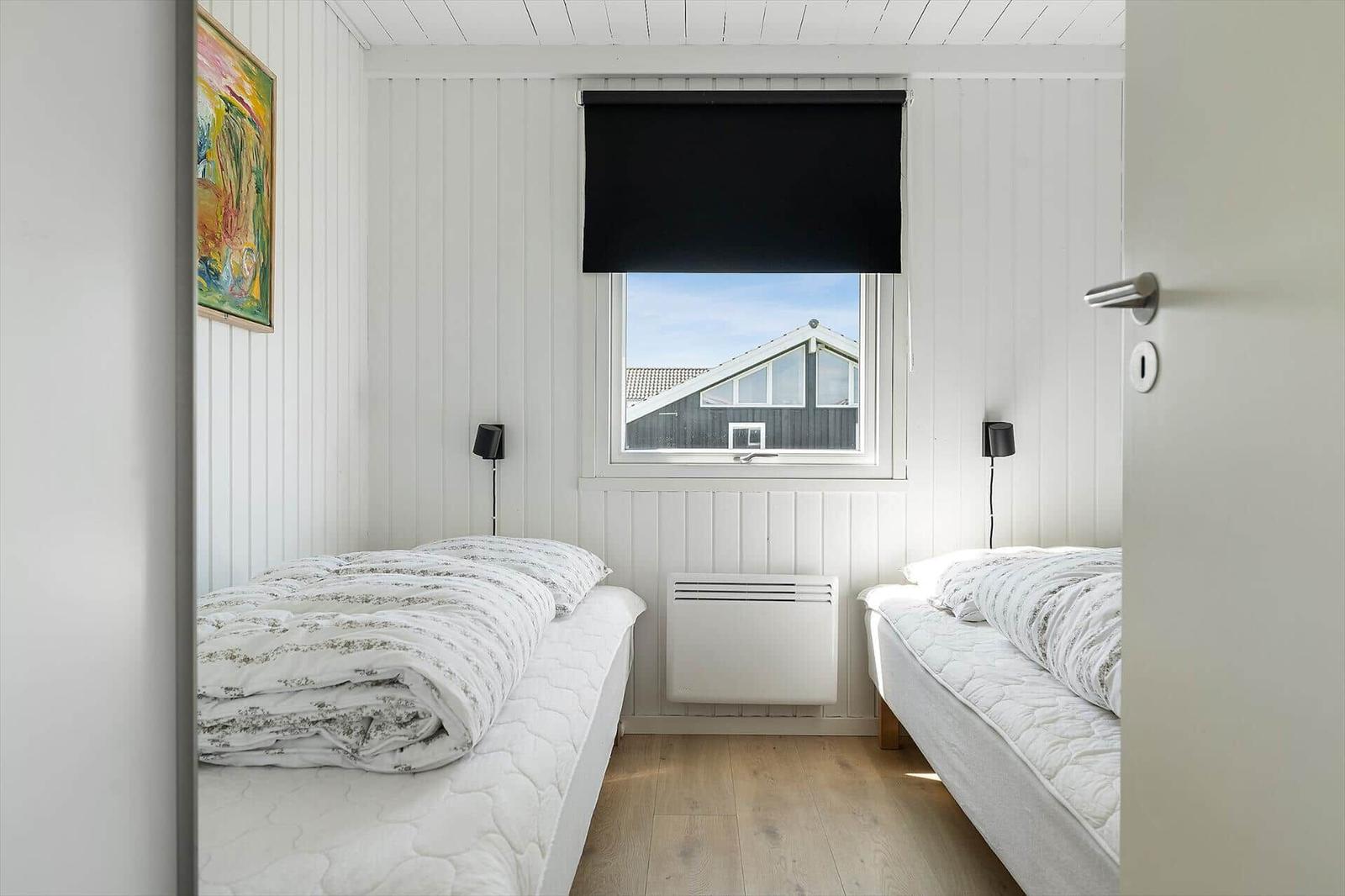 Two beds with white bedding are under a window with a view of a house.