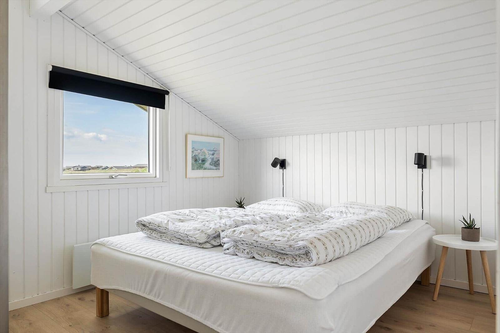 Bedroom with double bed, window, and white walls.