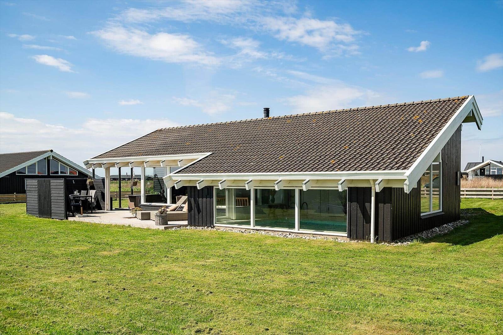 Modern villa with pool and terrace in green garden under blue sky.