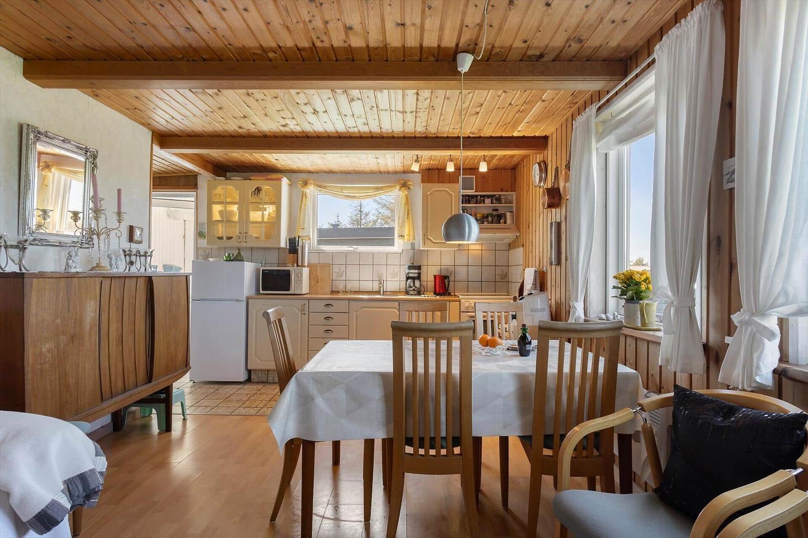 Dining room with wooden floor, table with chairs, and kitchen area in the background.