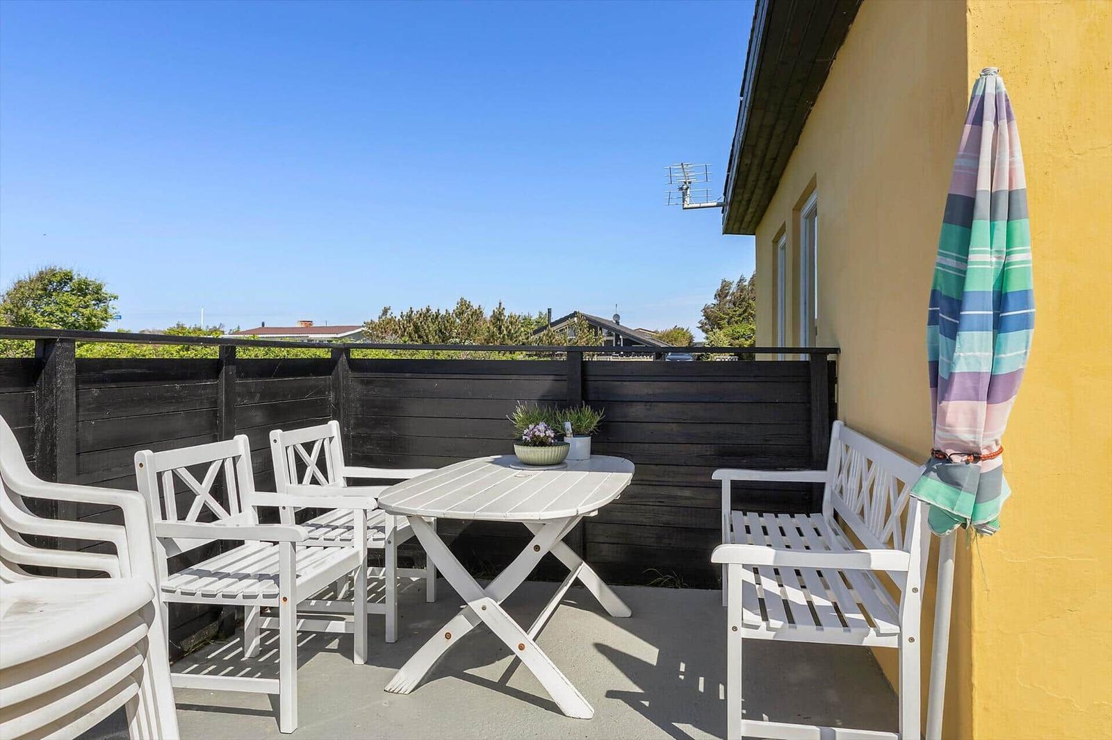 Terrace with white table and chairs, closed umbrella, and view of green areas.