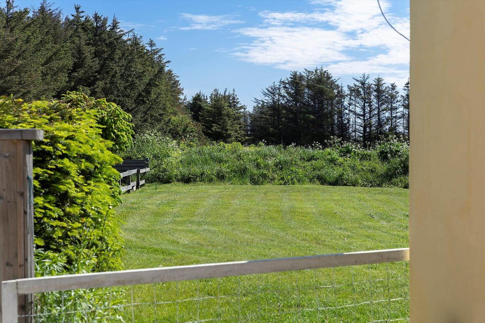 Green lawn area with wooden fence and forest in background under blue sky.