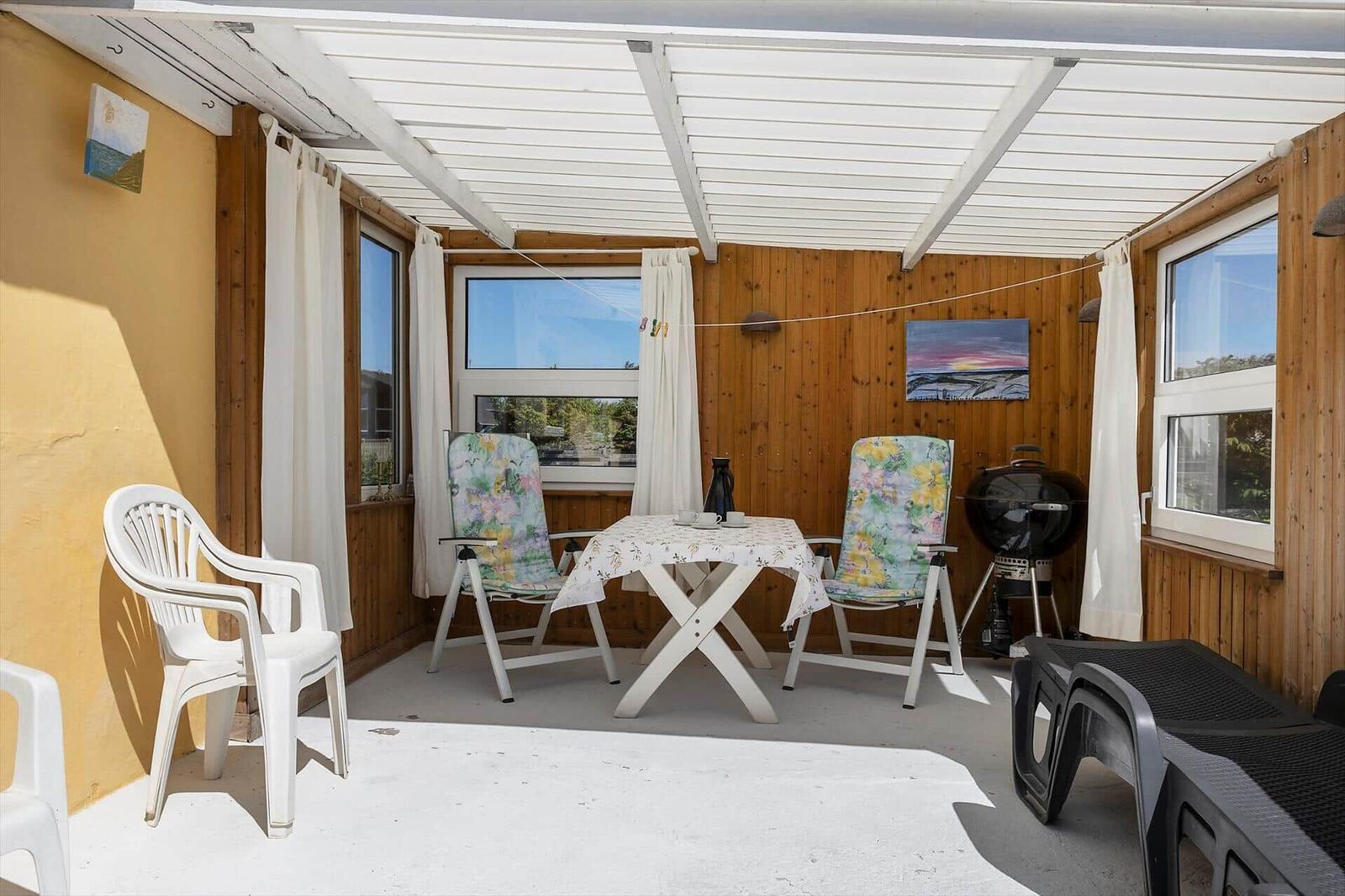 Patio with table, two chairs, grill, and lounge chairs under roof.
