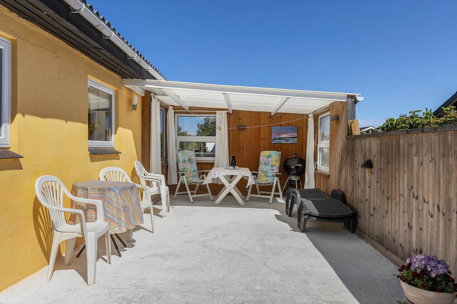 Terrace with table, chairs, sun loungers, and grill under awning.